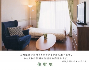 居室内観。ベッド、ソファ、テレビを備えた明るい個室。
